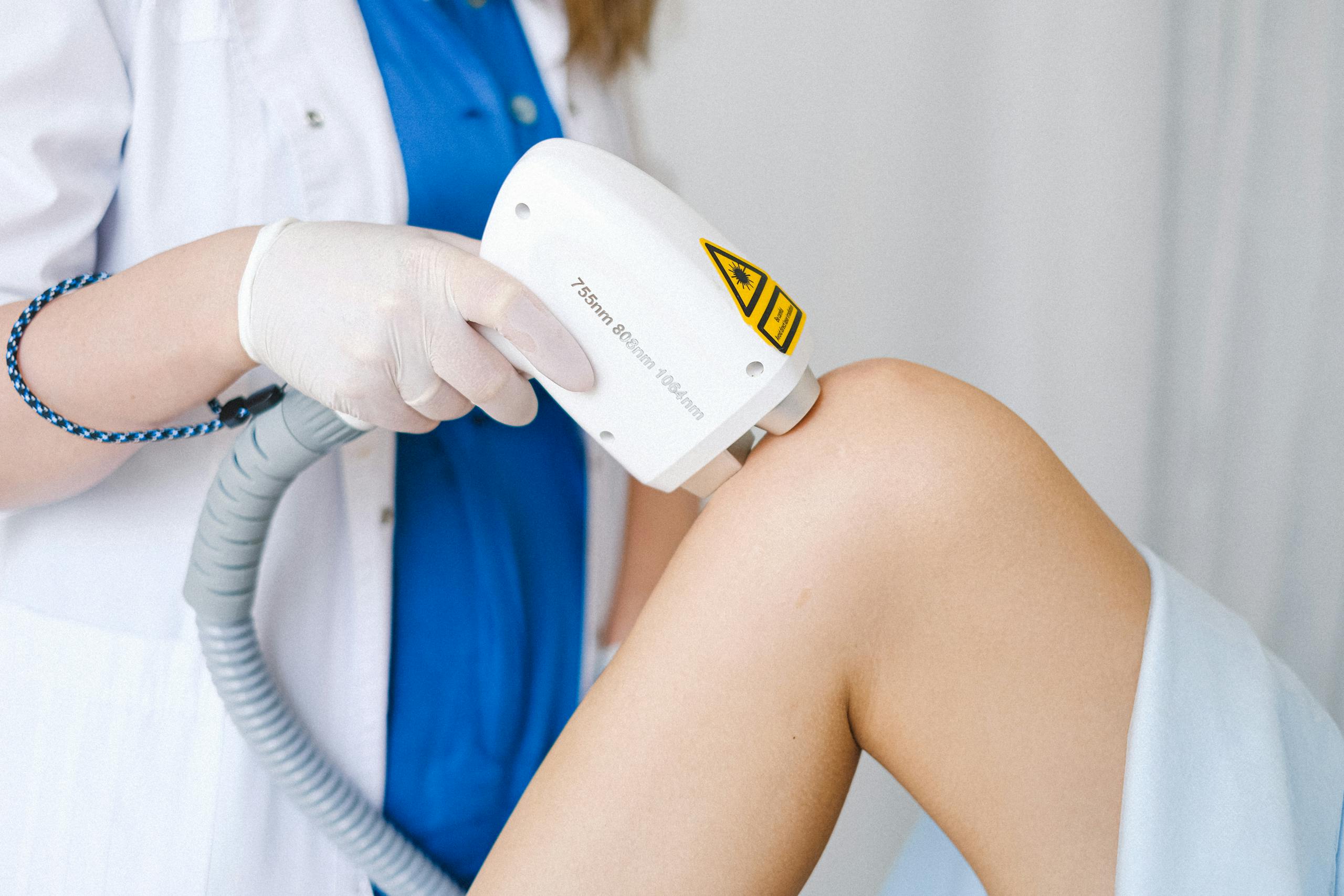 Crop unrecognizable cosmetologist in medical uniform using probe while doing low level laser therapy to calm patient in beauty salon